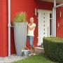 Garantia 2in1 Wasserbehälter in Zinkgrau mit Pflanzschale und Frau im Garten.