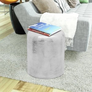 Runder, silberner Hocker/Beistelltisch aus gehämmertem Aluminium mit Büchern, neben grauem Sofa auf Teppich.