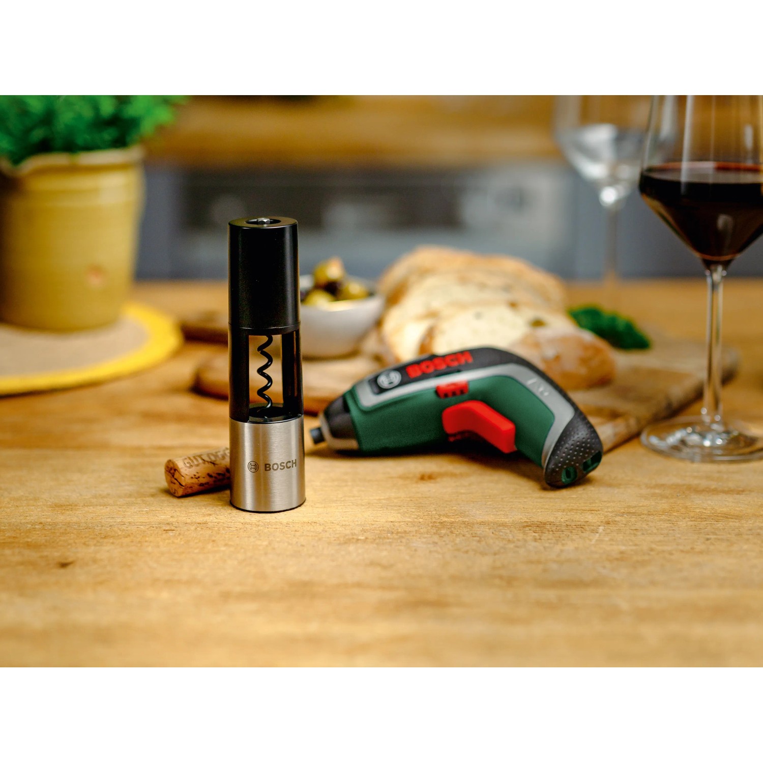 Bosch IXO 7 Akkuschrauber-Set mit Korkenzieher-Aufsatz auf Tisch mit Wein und Brot.