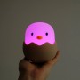 Dimmbares LED Nachtlicht Eggy Egg in Kükenform, leuchtend pink, in Hand gehalten.