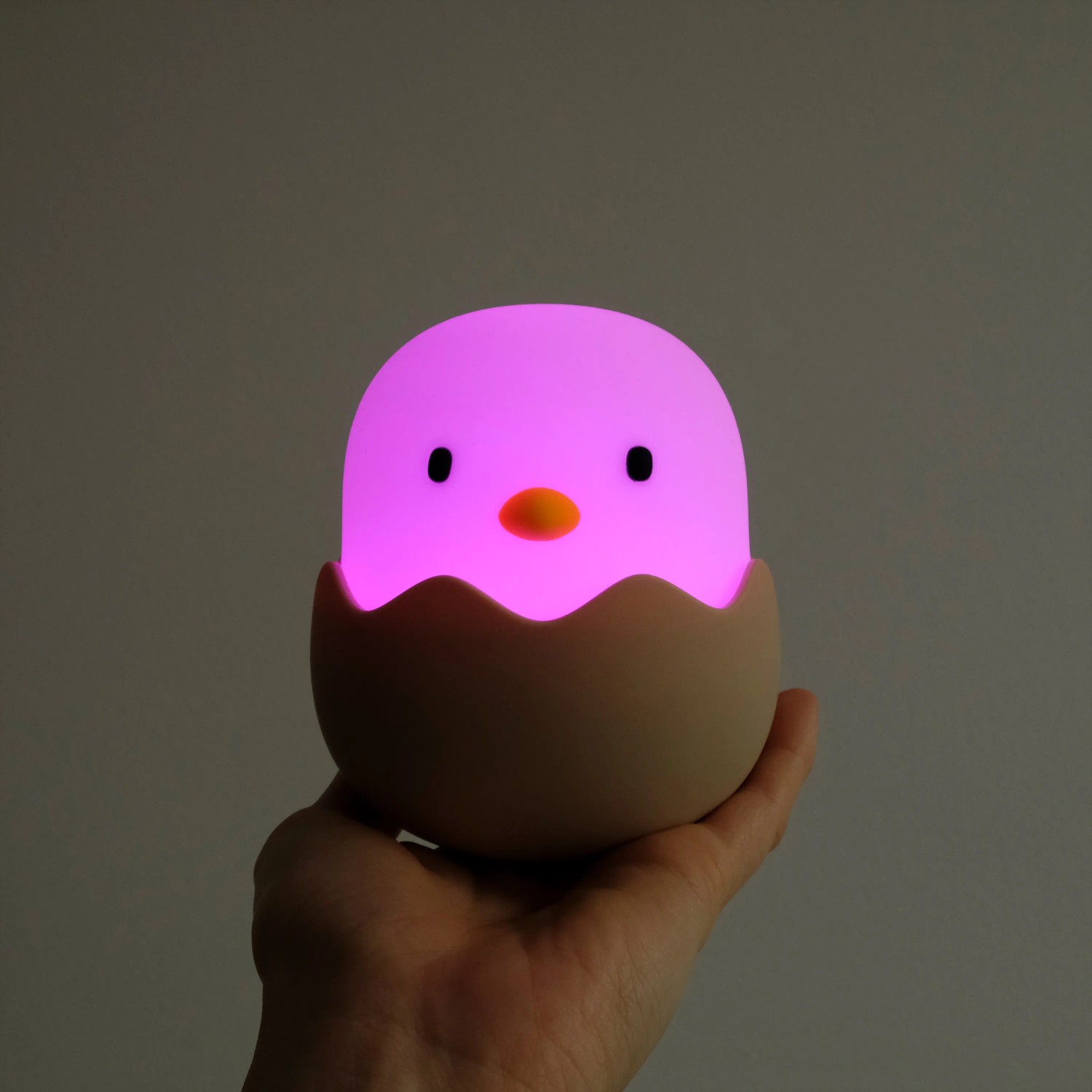 Dimmbares LED Nachtlicht Eggy Egg in Kükenform, leuchtend pink, in Hand gehalten.
