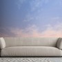 Fototapete Wolken in Blau, Weiß und Grau hinter einem Sofa. Romantische Vliestapete für Wohnzimmer.