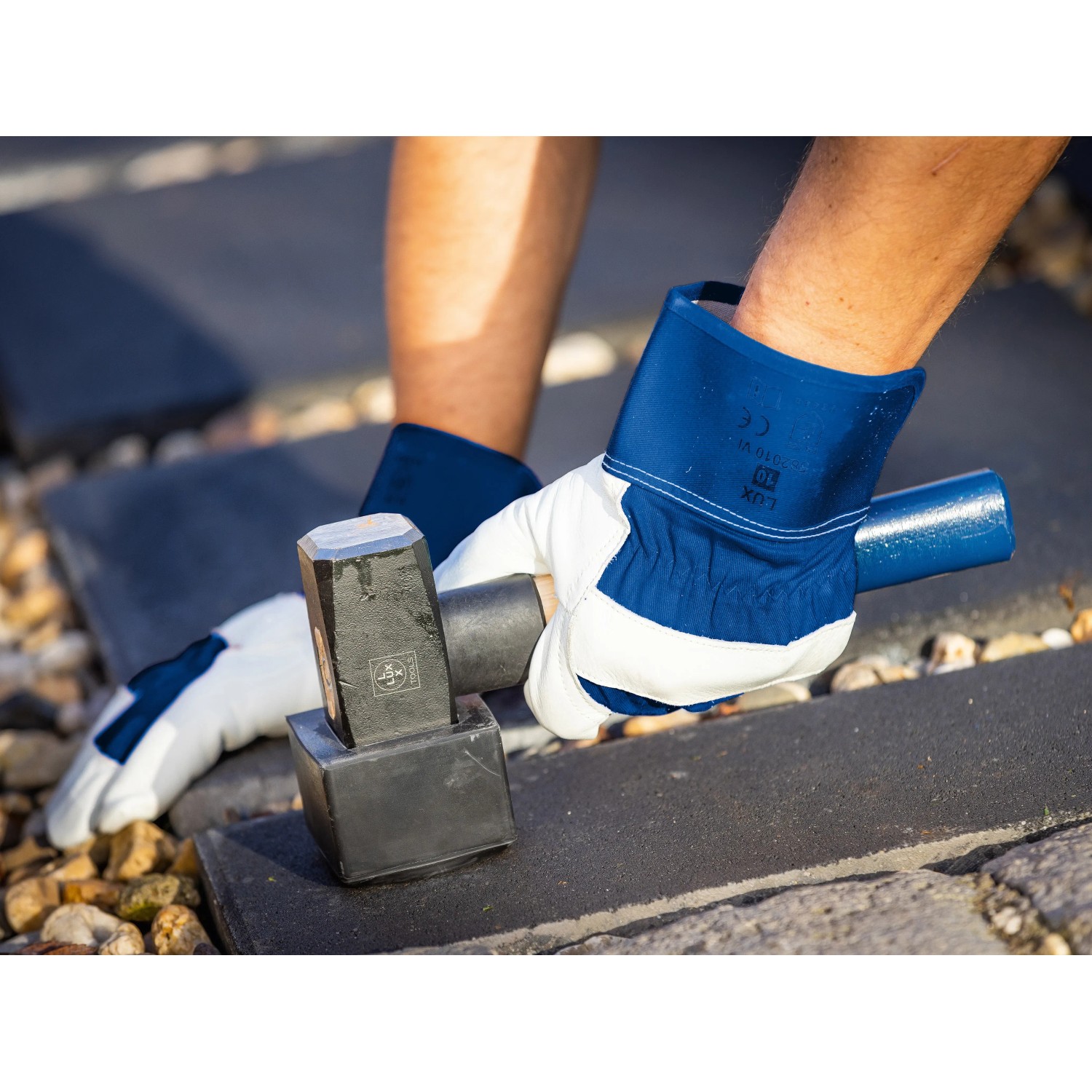 Hände mit LUX Arbeitshandschuhen aus Leder beim Pflastern mit Hammer.