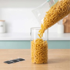 Transparentes Vorratsglas wird mit Fusilli Nudeln gefüllt. Schwarze Etiketten liegen auf Holztisch. Ideal für luftdichte Aufbewahrung in der Küche.