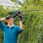 Mann schneidet Hecke mit Bosch Akku-Heckenschere Universal Hedge Cut 18-55. Gartengerät in Grün und Schwarz.