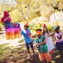 Kind mit Augenmaske schlägt mit buntem Stab auf Pinata im Garten. Pinata Zubehör Set für Spiel & Spaß.
