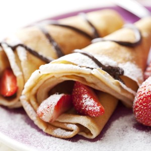 Süße Crêpes mit Erdbeeren und Schokoladensoße auf einem Teller.