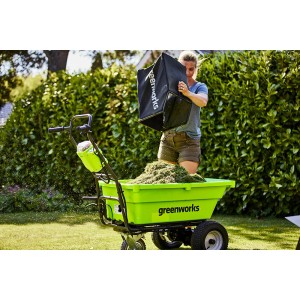 Grüne Greenworks Akku-Schubkarre G40GC mit Gras befüllt, Frau leert Fangkorb.