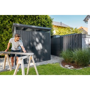 Floraworld Metall-Gerätehaus in Anthrazit mit Mann beim Aufbau im Garten.