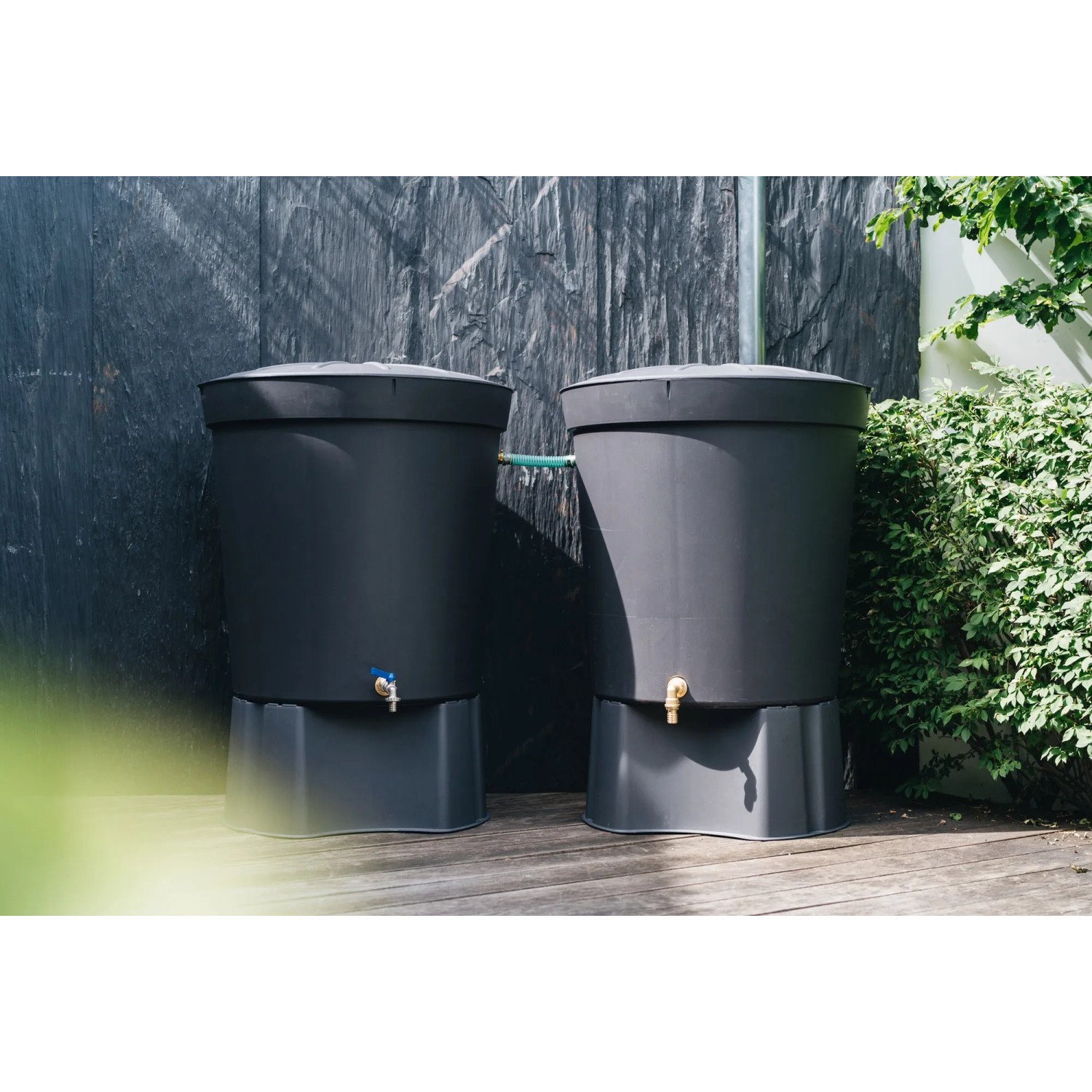 Zwei graue Regentonnen mit Messing-Anschluss-Set im Garten.