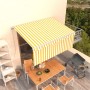 Gelb-weiße gestreifte Markise mit Rollo auf Balkon, schützt Esstisch und Grill vor Sonne. Manuell einziehbar, 3,5x2,5m.