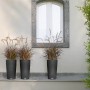 Drei graue Lechuza Cilindro Cottage Pflanzsäulen mit Bepflanzung vor einer Hauswand.