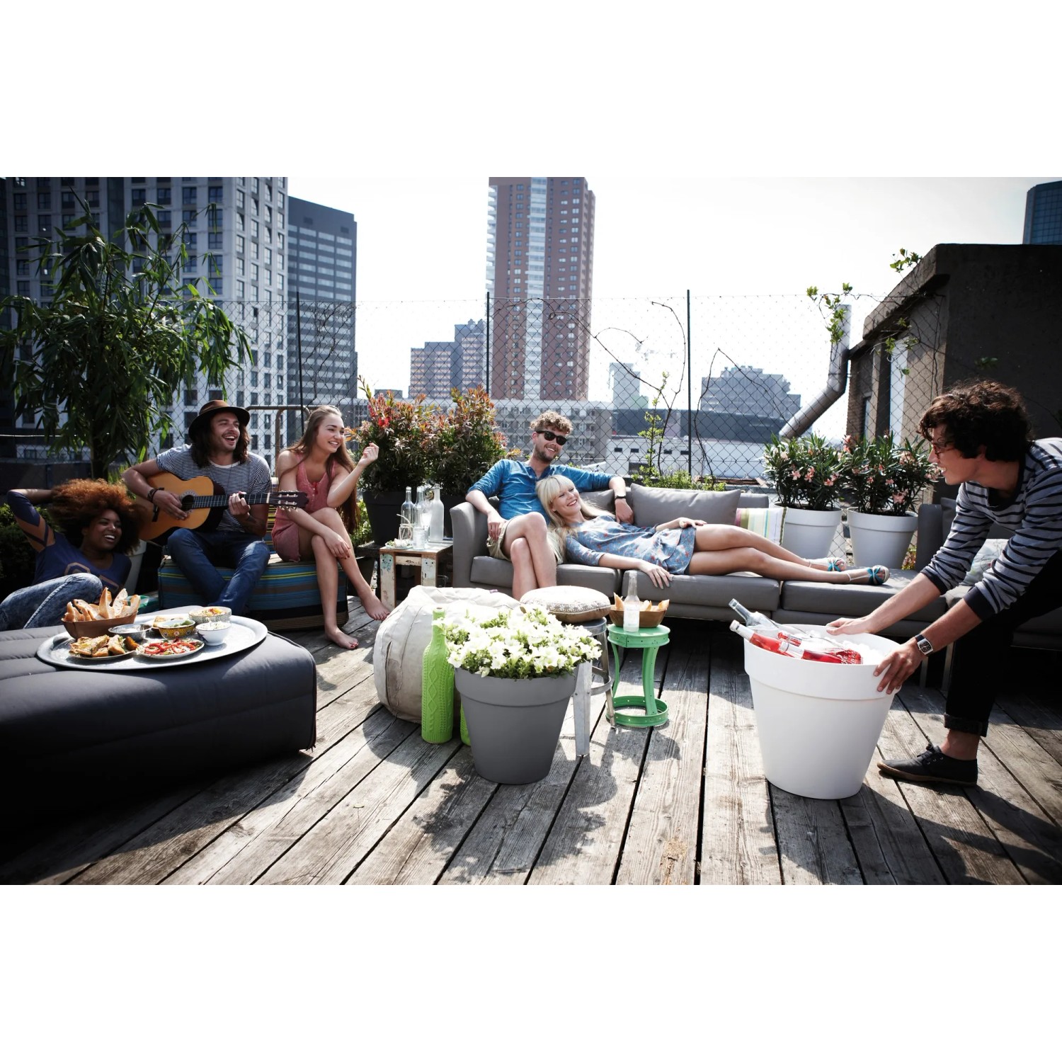 Anthrazitfarbener Elho Blumentopf Loft Urban mit Rollen (Ø 40 cm) auf einer Dachterrasse mit entspannten Menschen.