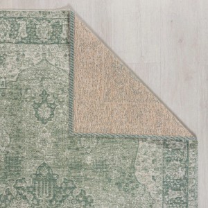 Grüner Vintageteppich mit antikem Persermuster. Eine Ecke ist umgeschlagen und zeigt die Unterseite auf hellem Holzboden.
