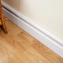 Weißes D-Line Kabelkanal-Set (10-teilig) an Wand über einer weißen Fußleiste auf Laminatboden.
