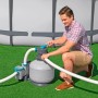 Mann schließt graue Sandfilteranlage mit Schläuchen an Pool an. Filterpumpe auf grünem Rasen für Poolreinigung.