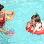 Kind mit rotem Freds Swim Academy Schwimmreifen im Pool mit Mutter.