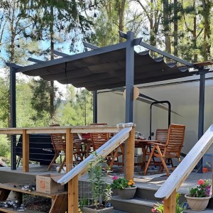 Dunkelgraue Aluminium Pergola mit ausziehbarem Schiebedach auf Holzterrasse. Bietet Sonnenschutz im Garten.