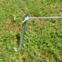 Silberfarbener V-förmiger Zelthering aus verzinktem Stahl im grünen Gras, mit befestigter Spannleine. Camping Zubehör.