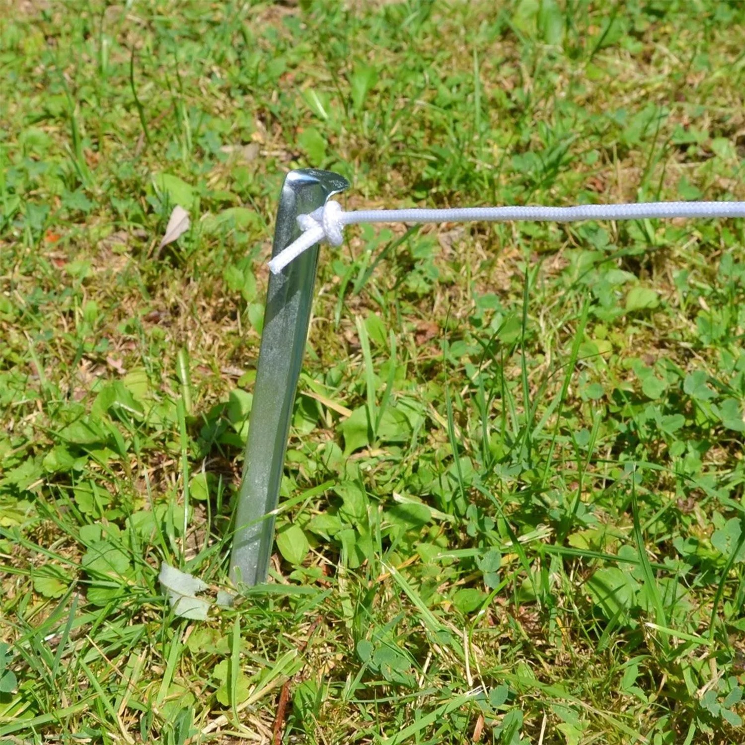 Silberfarbener V-förmiger Zelthering aus verzinktem Stahl im grünen Gras, mit befestigter Spannleine. Camping Zubehör.