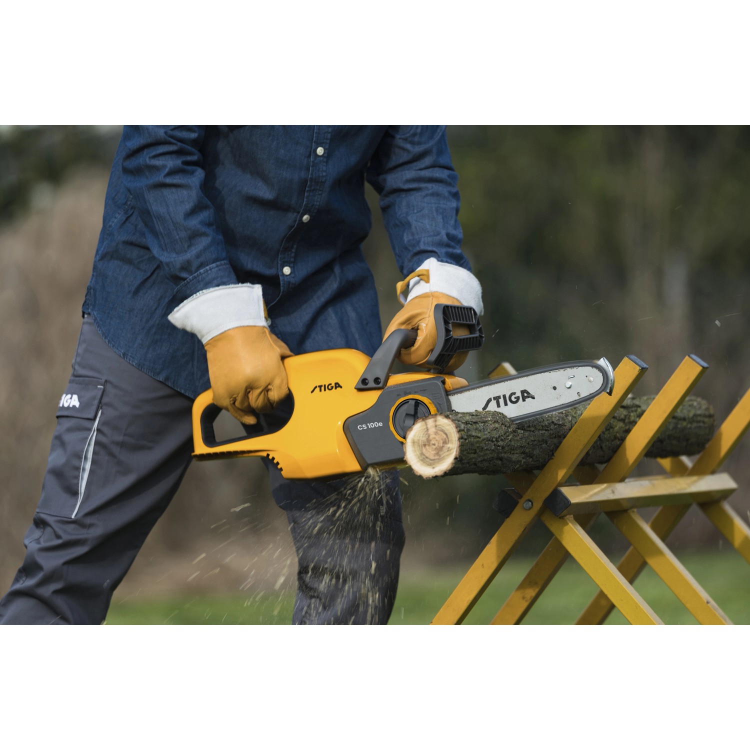 Stiga Akku-Kettensäge CS 100er beim Sägen von Holz auf einer gelben Holzkonstruktion.