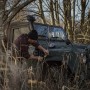Mann befestigt Tesa Reparaturband am Kotflügel eines Geländewagens im Wald.