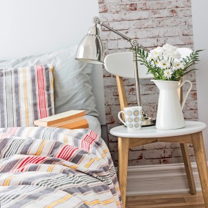 Schlafzimmer mit Klinker Tapete in Steinoptik, Bett und Nachttisch mit Lampe und Blumen.
