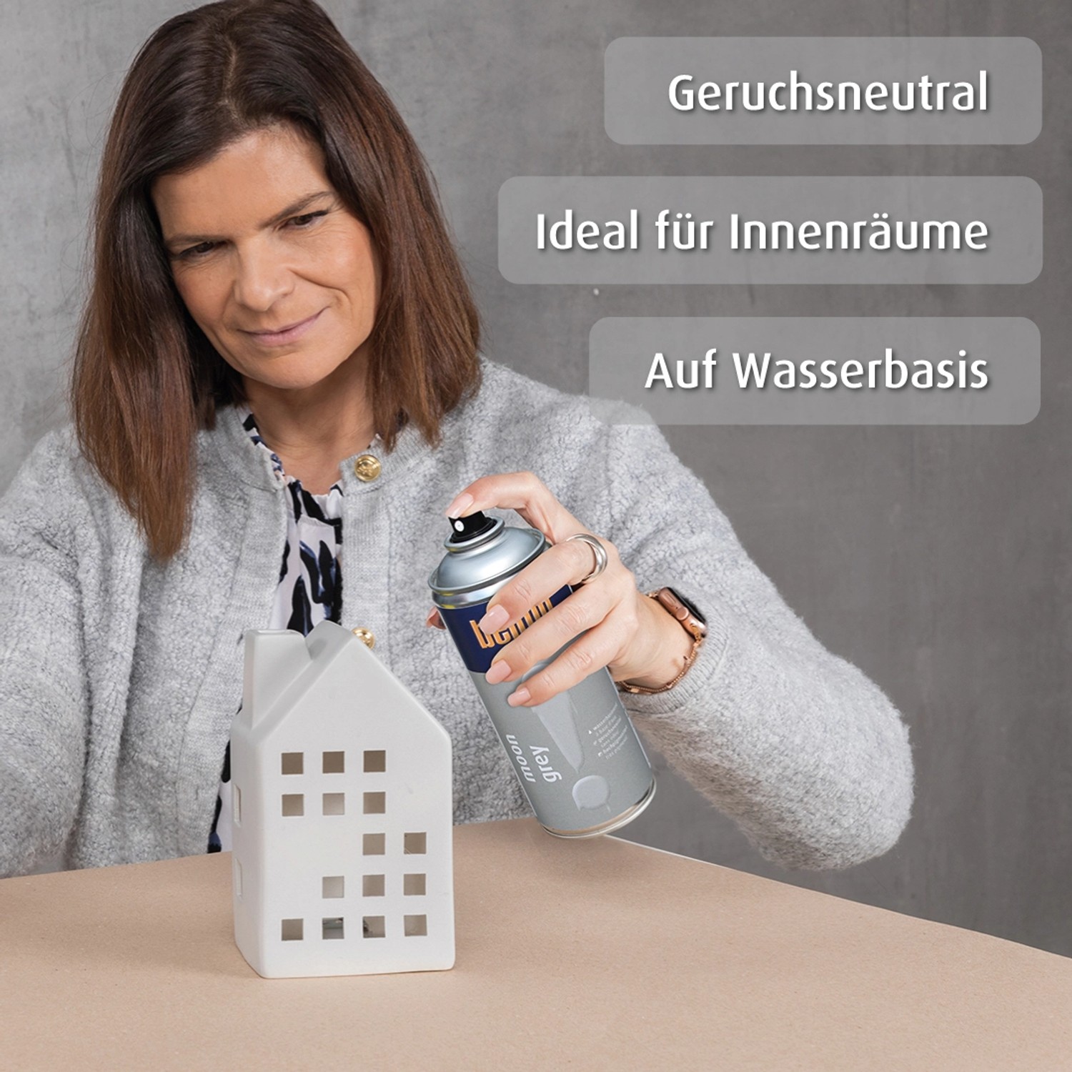 Frau sprüht belton Buntlack Perfect Moon Grey seidenmatt auf Deko-Haus. Buntlack-Spray für Innen & Außen.