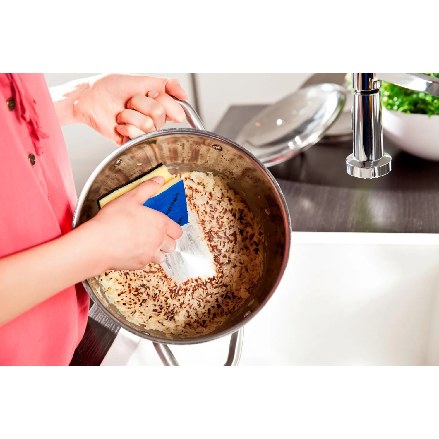 Vileda Glitzi Plus Topfreiniger im Einsatz: Frau reinigt Topf mit Speiseresten in der Küche.