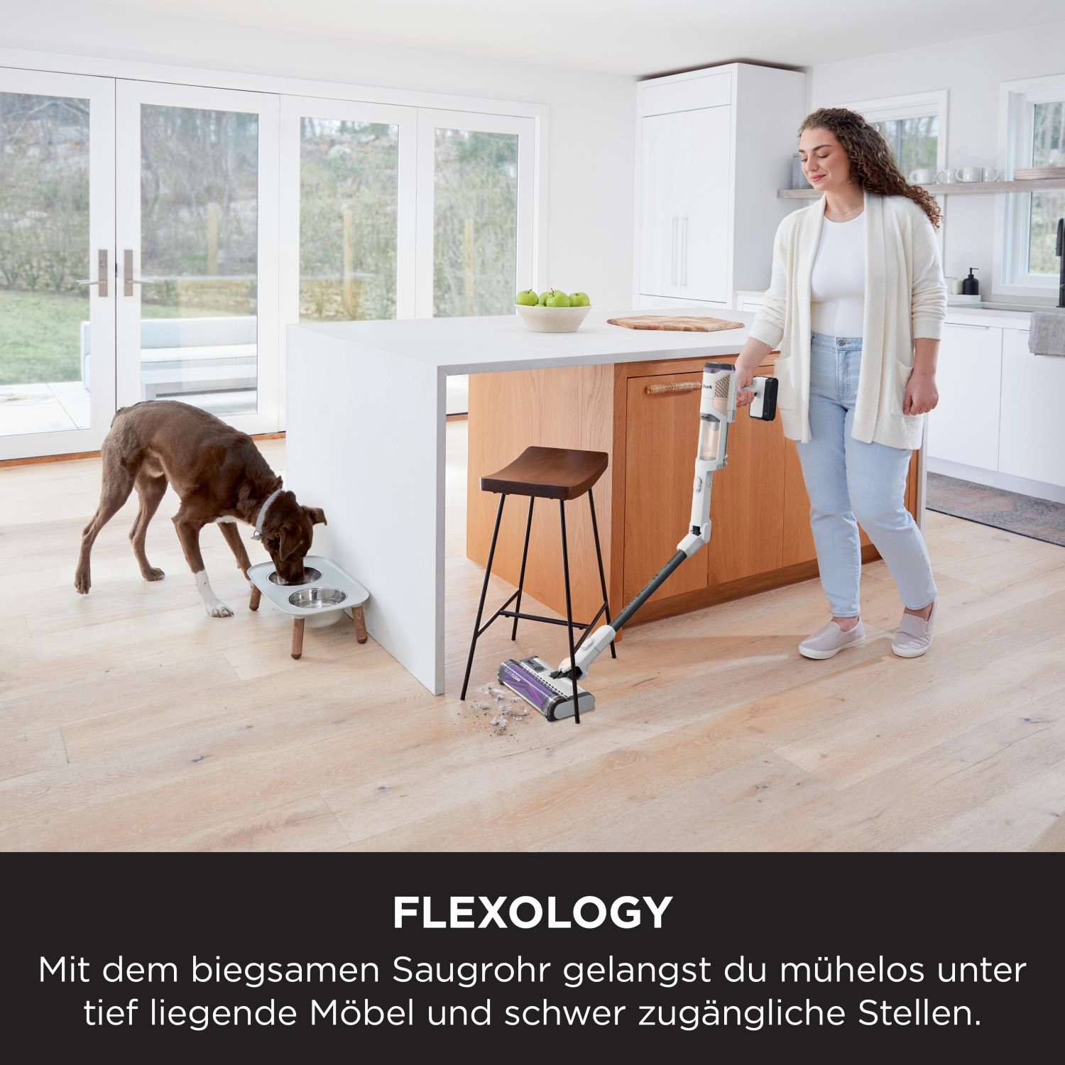 Shark Stielsauger Detect Pro IW1611EU im Einsatz, Frau saugt Krümel neben Hund, der frisst.