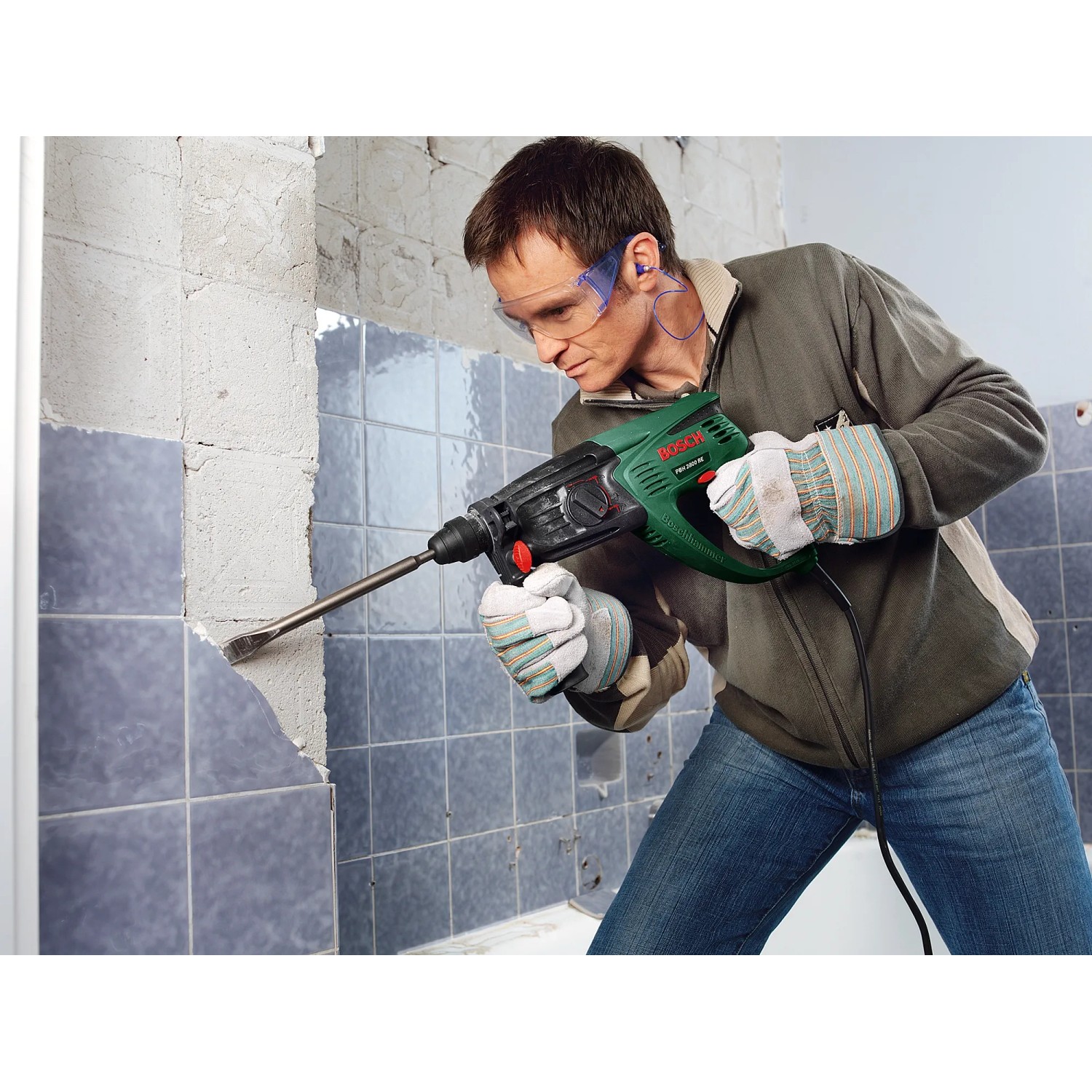 Mann arbeitet mit Bosch Bohrhammer PBH 2800 RE an Fliesenwand. Der Bohrhammer ist grün und schwarz.