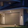 Moderne Philips Hue Resonate LED-Außenwandleuchte in Schwarz mit Lichtkegel an Hauswand.