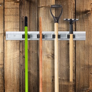 Silberne Aluminium-Gerätehalterleiste mit 4 schwarzen Klemmen an Holzwand, hält Besen, Schaufel und Rechen. Ordnungssystem für Gartenwerkzeuge.