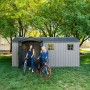Graues Lifetime Gerätehaus Idaho mit zwei Frauen und Fahrrädern im Garten.