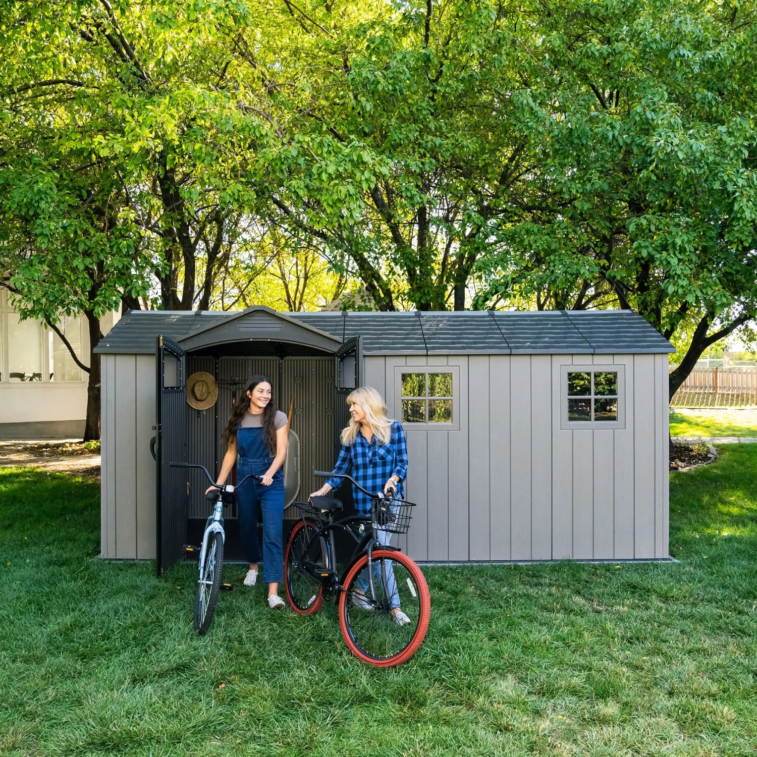 Graues Lifetime Gerätehaus Idaho mit zwei Frauen und Fahrrädern im Garten.