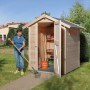 OBI Holz-Gartenhaus Kompakt mit Satteldach, 152x171 cm, naturbelassen, mit offener Tür und Frau mit Rechen.