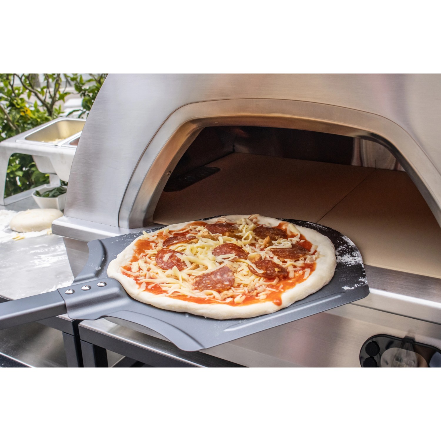 Buschbeck Pizzaofen X1 mit Pizza auf Schieber vor dem Ofen. Gas- und Holzbetrieb möglich.