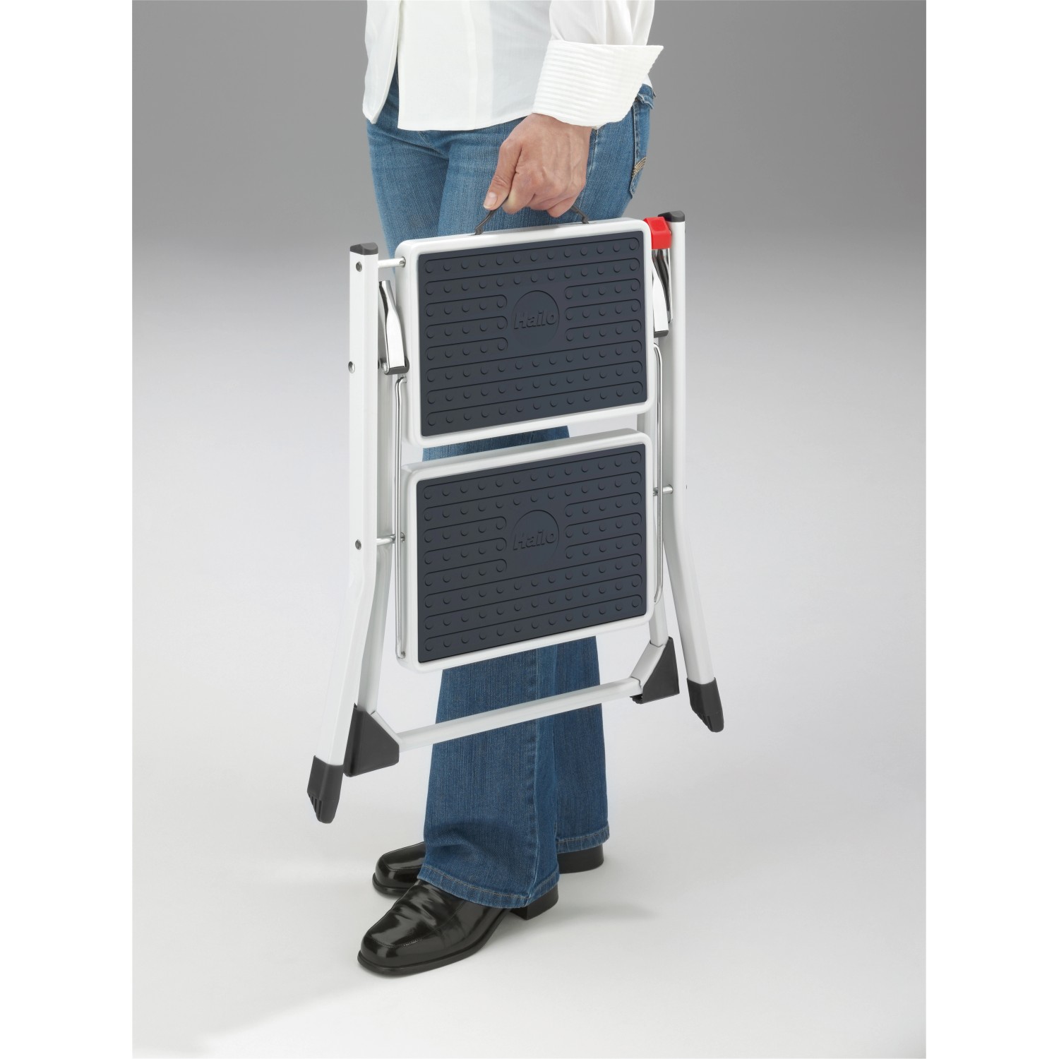 Zusammengeklappter Hailo Klapptritt Mini in Weiß-Anthrazit mit 2 Stufen und Anti-Rutsch-Matten wird von einer Person getragen.