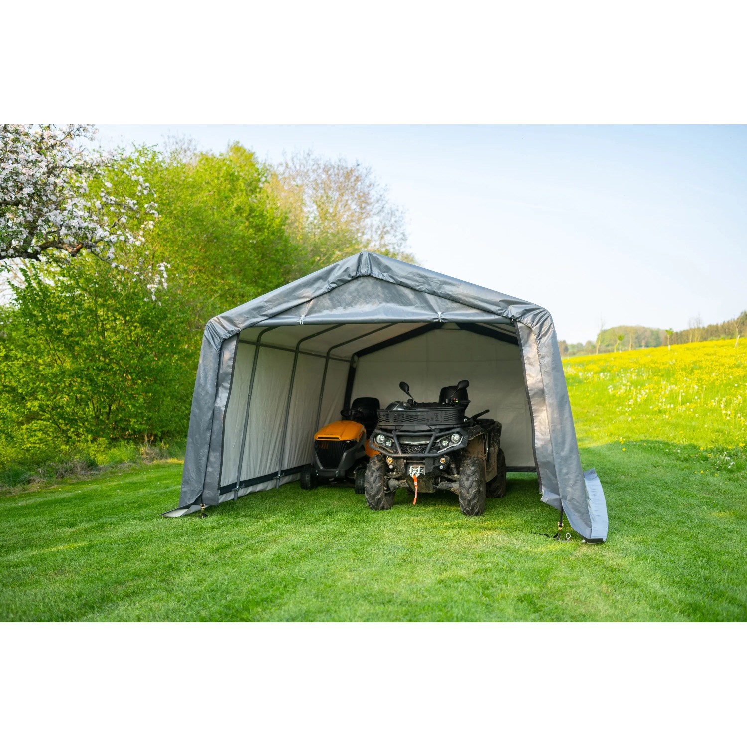Graue ShelterLogic Garage-in-a-Box mit Rasentraktor und Quad im Grünen.
