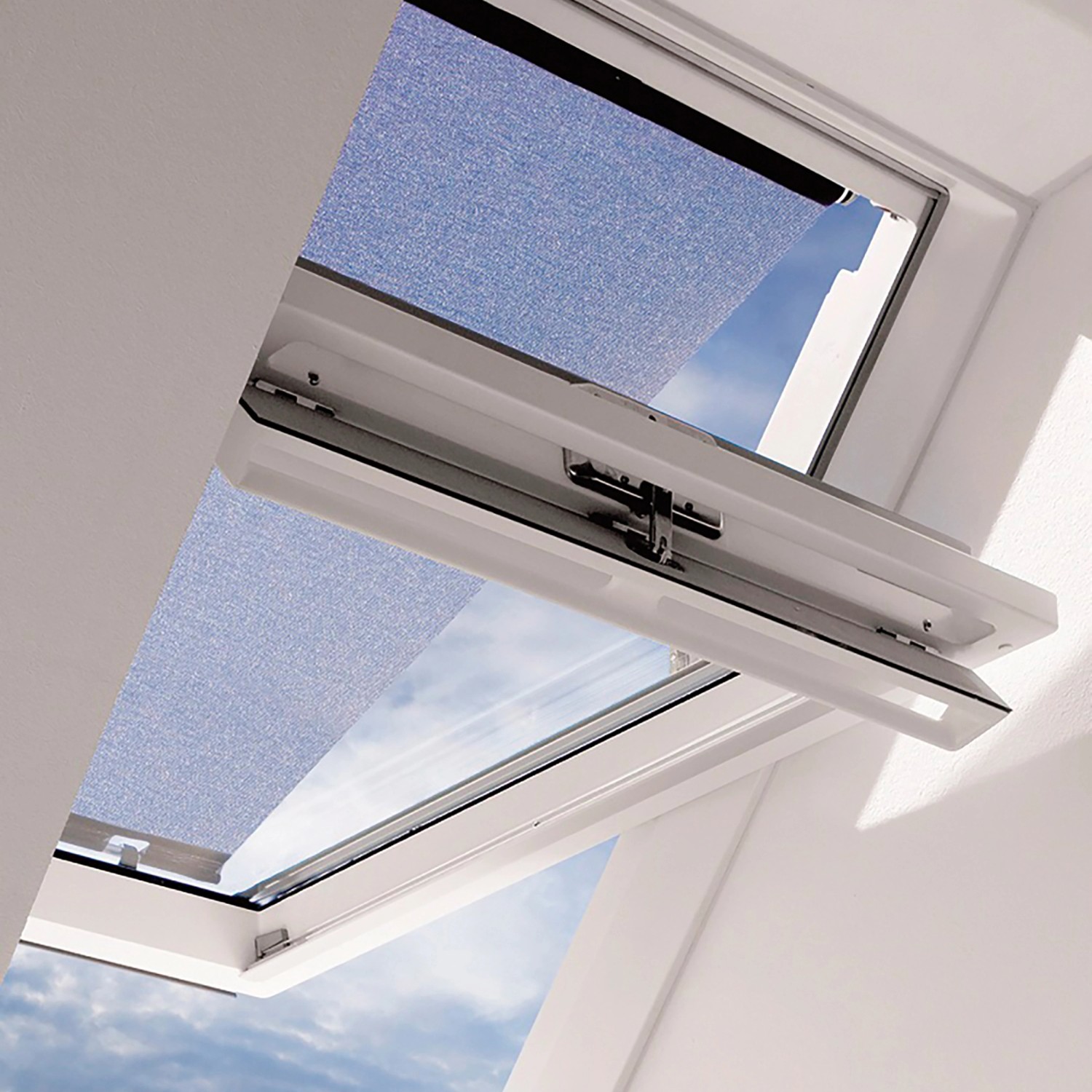 Velux Hitzeschutz-Markise MHL CK00 am Dachfenster, teilweise geöffnet, blauer Himmel sichtbar.