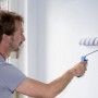 Mann streicht Wand mit Knauf Easy Putz Schneeweiß und Farbwalze. Strukturierter Innenputz.