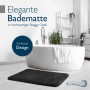 Schwarze rechteckige Hochflor Badematte (50x60cm) in Shaggy Optik vor weißer Badewanne. Rutschfest und zeitlos.
