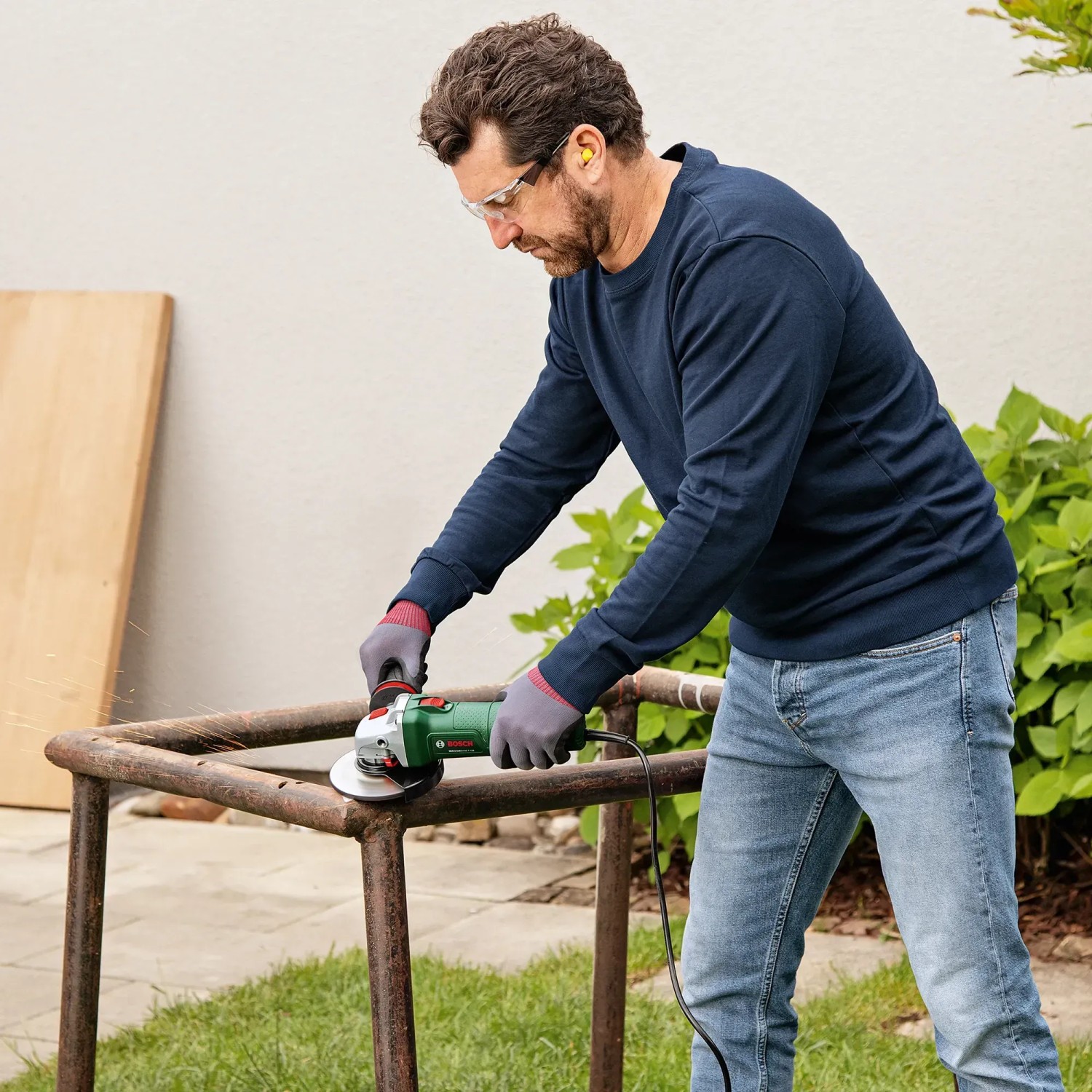 Mann schleift Metall mit dem Bosch UniversalGrind 850-125 Winkelschleifer im Freien.