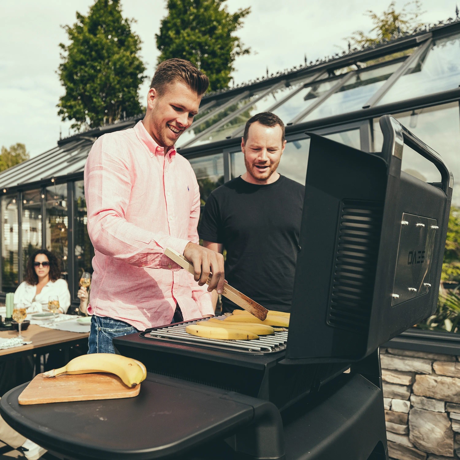 Zwei Männer grillen Maiskolben auf dem Severin Stand-Elektrogrill Sevo GTS im Garten.