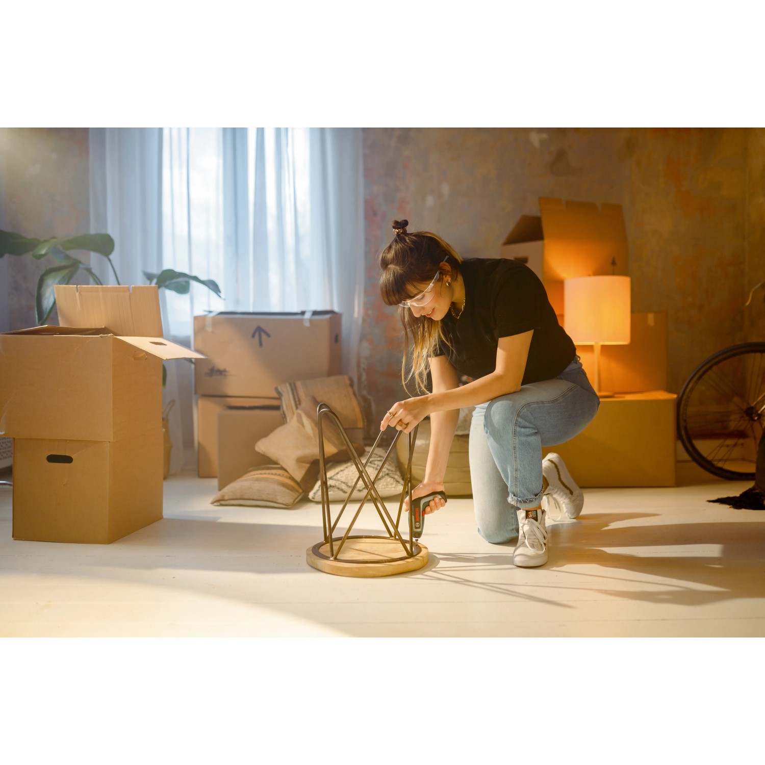 Frau montiert Möbel mit Bosch IXO 7 Akkuschrauber-Set in Umzugsumgebung.