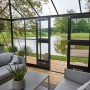 Begehbares Juliana Gewächshaus Grand Oase 18 in Anthrazit mit Doppeltür und Blick auf einen See.