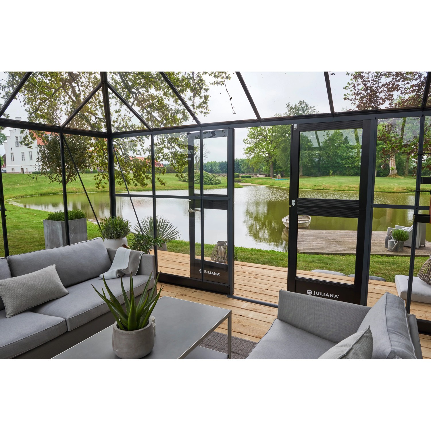 Begehbares Juliana Gewächshaus Grand Oase 18 in Anthrazit mit Doppeltür und Blick auf einen See.
