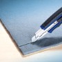 LUX Cuttermesser Comfort 100 mm schneidet grauen Stoff. Universalmesser mit blauem Griff.