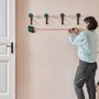 Frau benutzt Bosch Atino Linienlaser mit Maßband zum Ausrichten von Wandhaken.