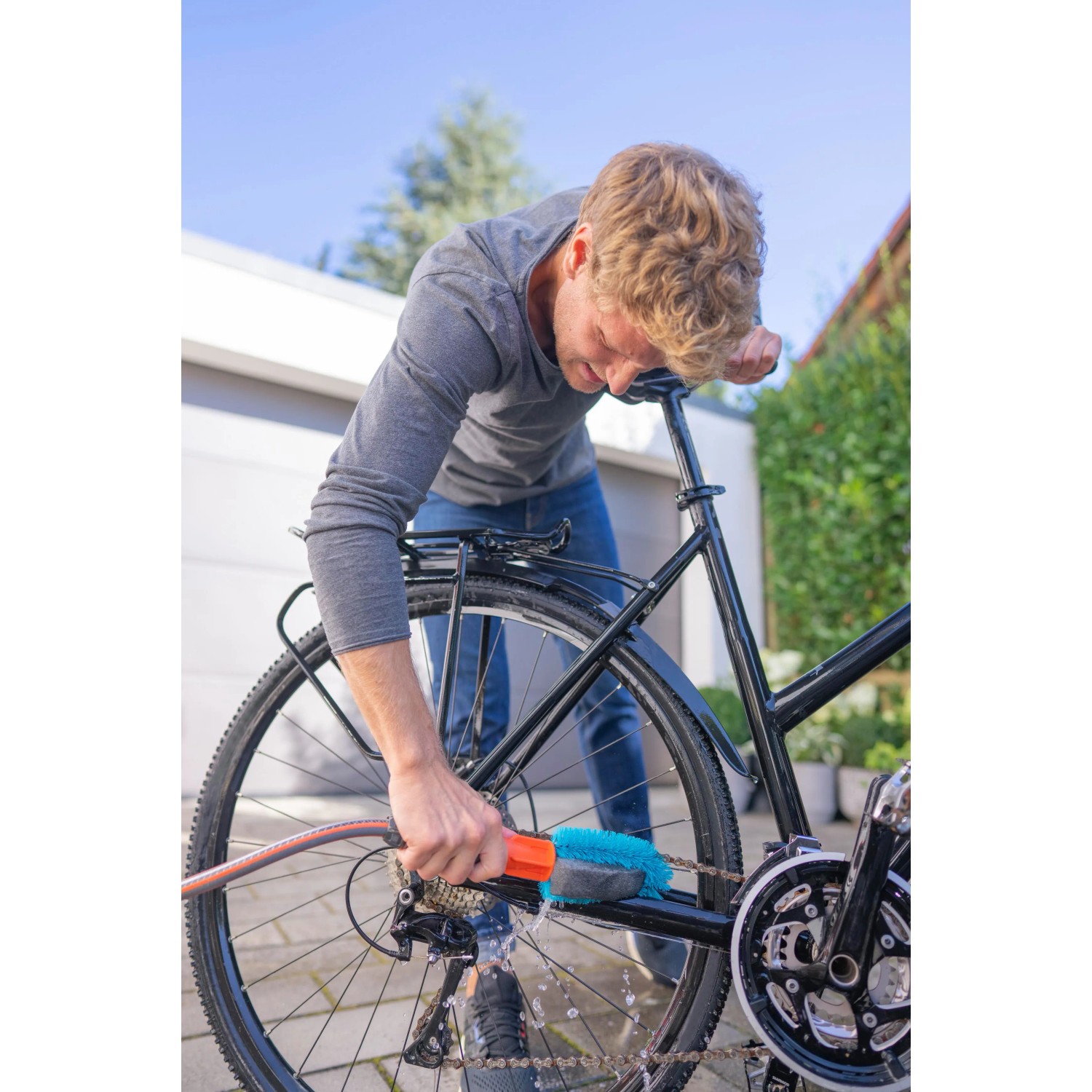 Mann reinigt Fahrradkette mit Gardena Cleansystem Fahrradbürste. Blaue Bürste mit Wasseranschluss.